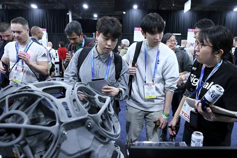 In a crowd of people three discuss an unseen item on a table just off camera.